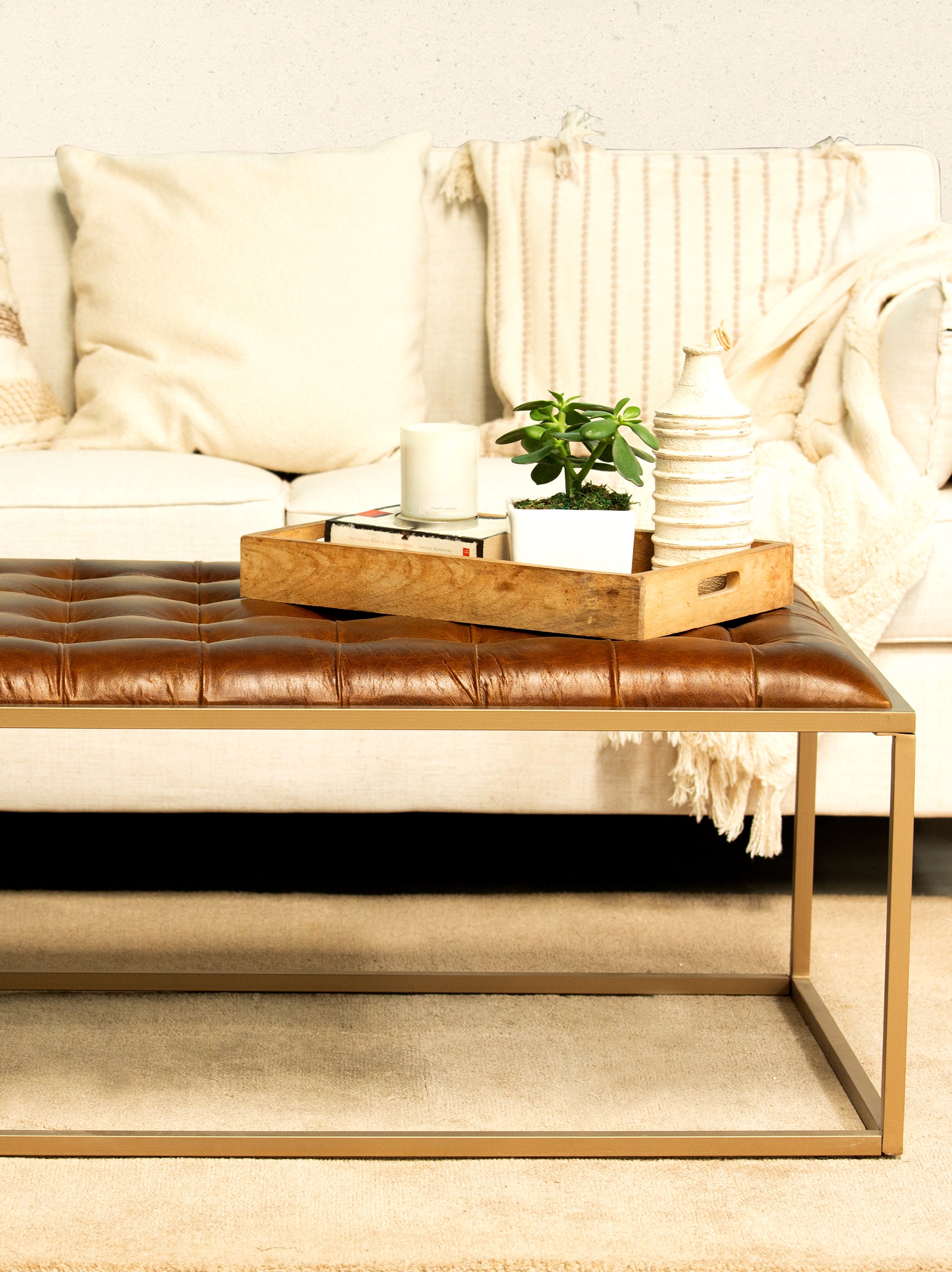 A brown leather coffee table with a golden finish iron base, featuring biscuit tufting and a decorative item on top, placed in a living room setting.