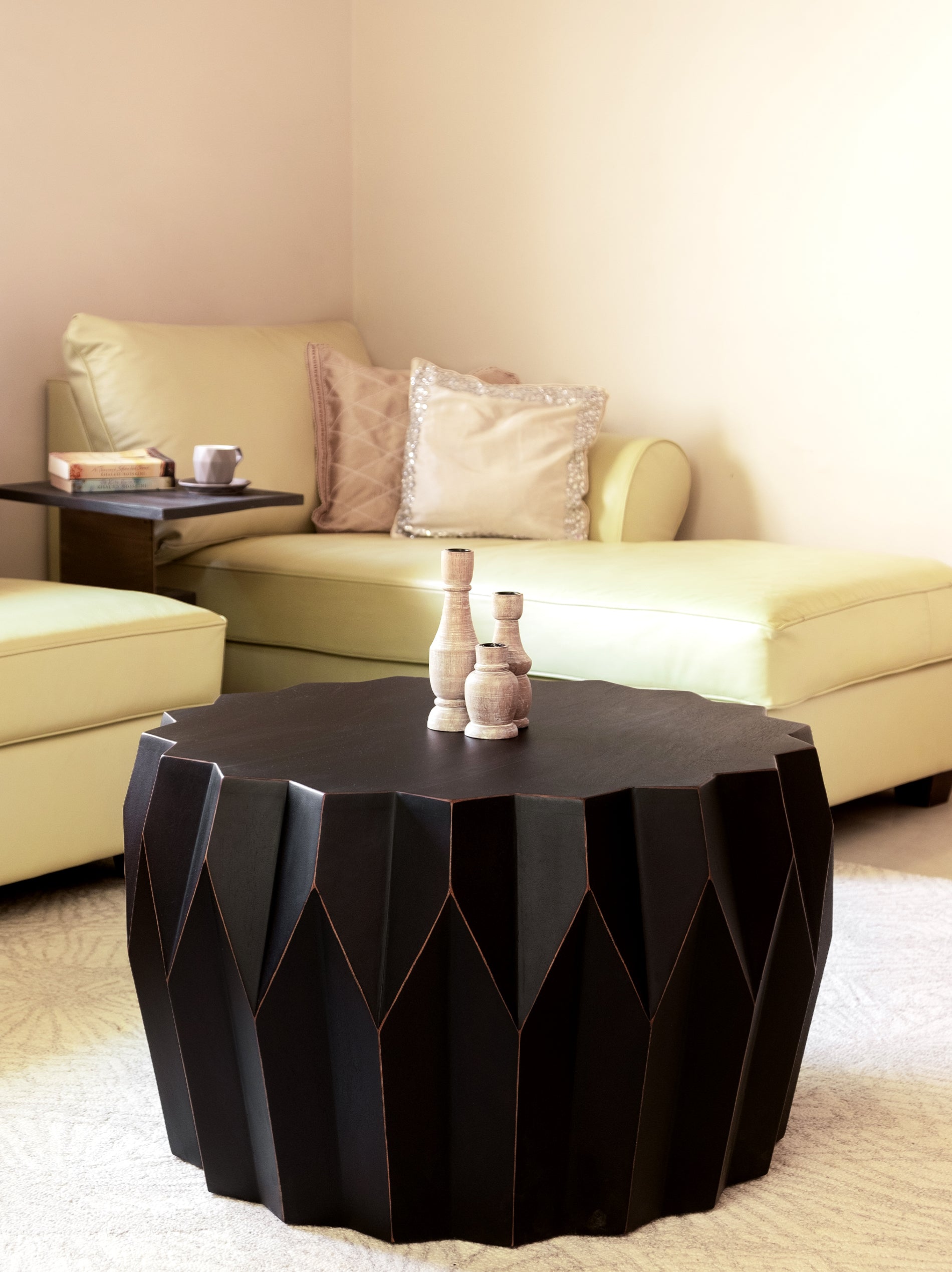 A round, black Chantell Coffee Table made of mango wood, with a geometric patterned base, placed in a living room setting.